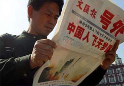Consumidor chino se deja fotografiar orgulloso mientras lee en un diario chino noticias sobre el primer vuelo espacial tripulado chino