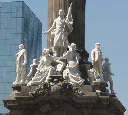 Conjunto escult&oacute;rico del basamento de la Columna de la Independencia. Don Miguel Hidalgo aparece al centro escoltado por dos estatuas de m&aacute;rmol de g&eacute;nero femenino que representan: a la izquierda, la Historia, sosteniendo un libro, y, a la derecha, la Patria, entregando un laurel de victoria. En las esquinas se aprecian las estatuas de Don Jos&eacute; Mar&iacute;a Morelos, a la izquierda,&nbsp;y Don Vicente Guerrero, a la derecha de la foto. Atr&aacute;s se alcanzan a distinguir las estatuas de Nicol&aacute;s Bravo y Xavier Mina